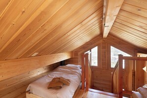 Una cabaña de madera con un entrepiso que tiene una cama, un ventanal y una escalera de madera.