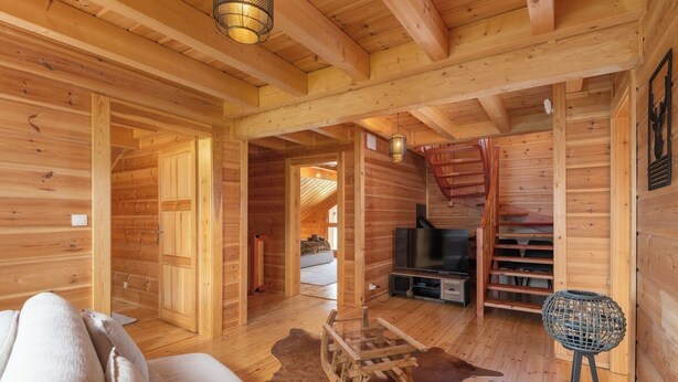 A wooden cabin interior with a sofa, a television, and a staircase.
