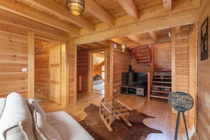 Interior de una cabaña de madera con sofá, televisor y escalera.