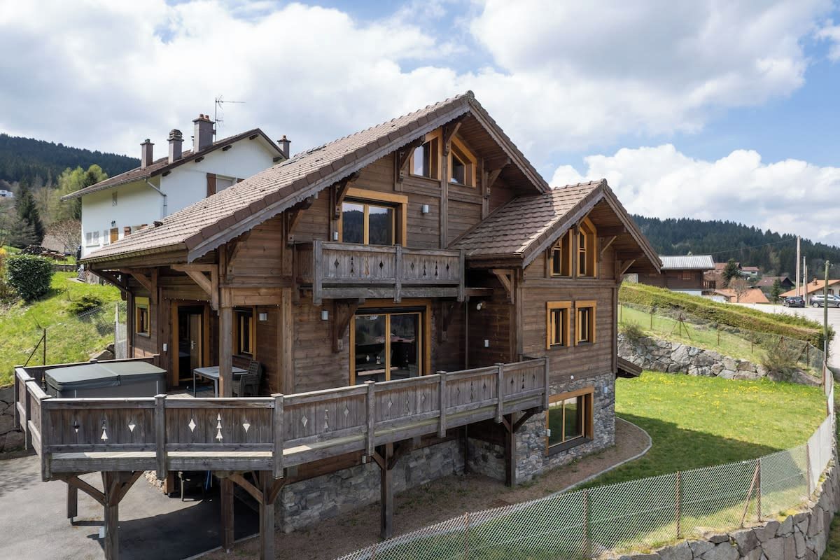 Een houten chalet met een balkon, stenen fundering en uitzicht op een bergachtig landschap.