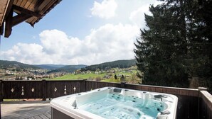 A hot tub on a wooden deck with a view of a valley and mountains.