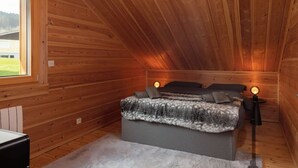 A bedroom with a sloped ceiling, a bed with a blanket, two bedside lamps, and a window.