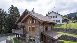 A two-story wooden house with a balcony, stone foundation, and a sloped roof.