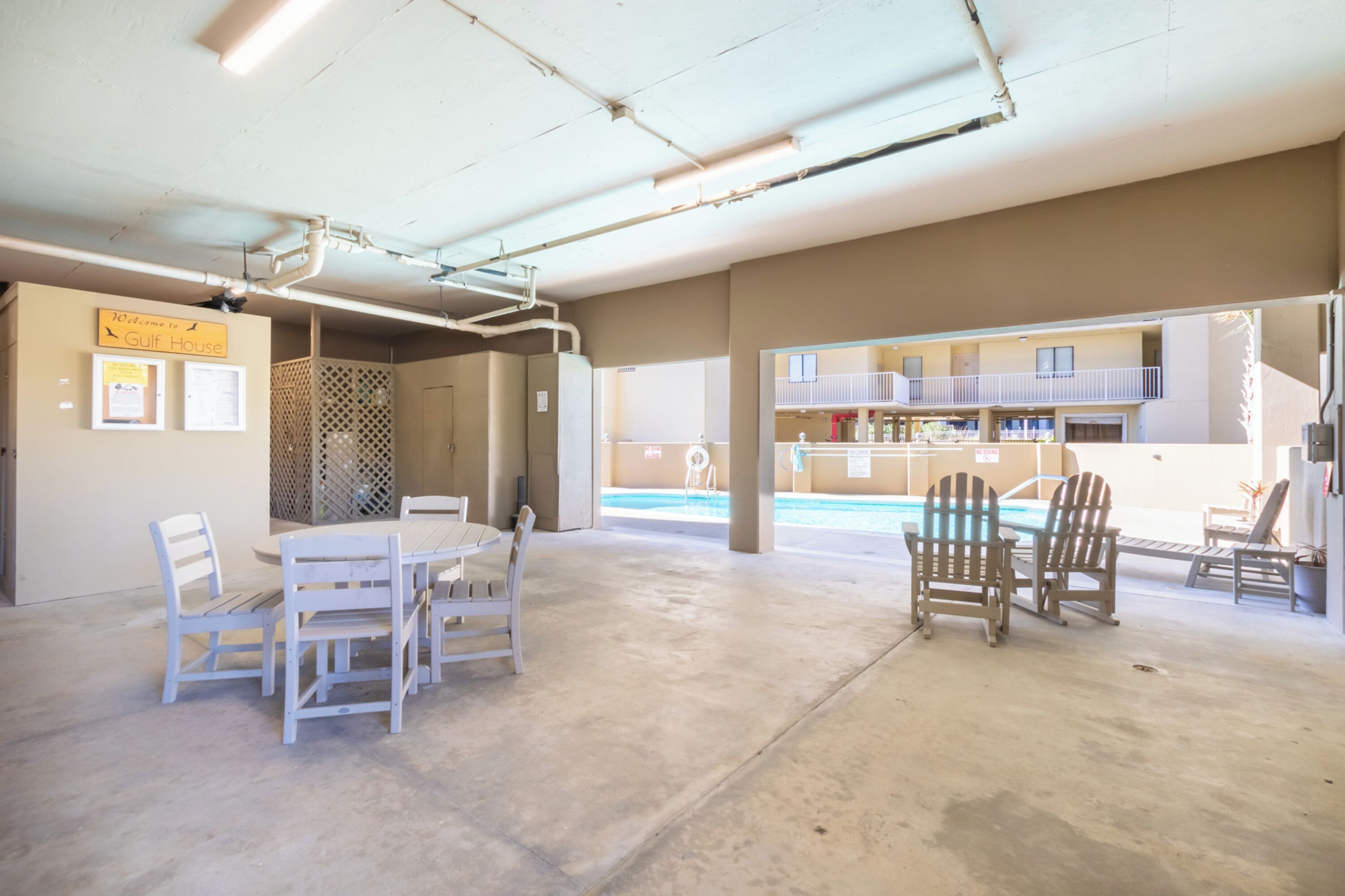 Un amplio espacio interior con piscina, sillas blancas y una mesa.