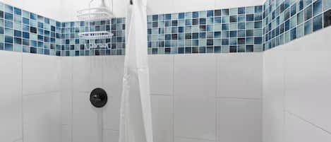 Una ducha con cortina blanca, un cabezal de ducha manual y un inodoro con dispensador de papel higiénico.