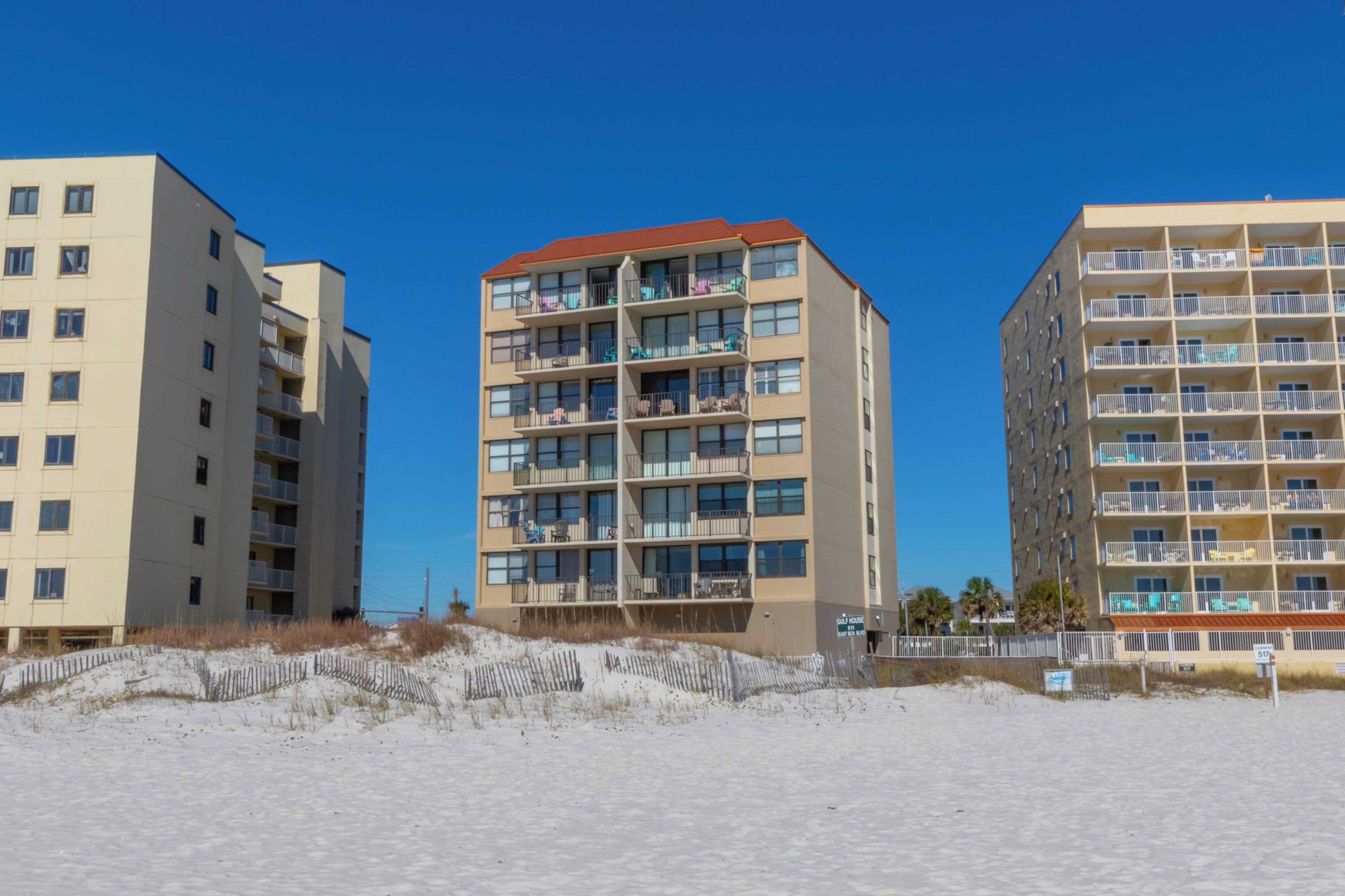 Ein Strandhotel mit mehreren Etagen, Balkonen und einem Sandstrand davor.