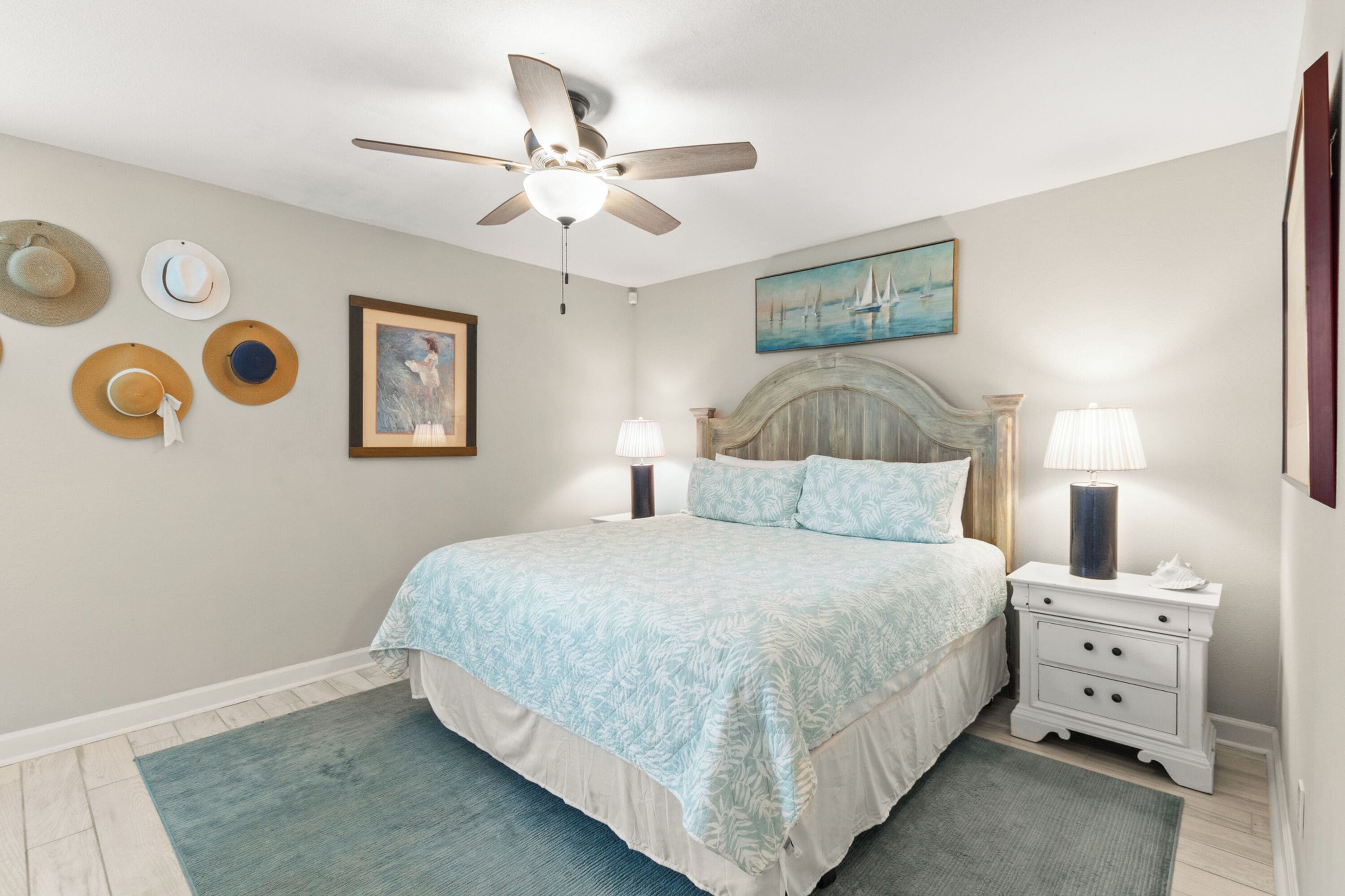 A bedroom with a bed, nightstands, a ceiling fan, and wall-mounted hats.