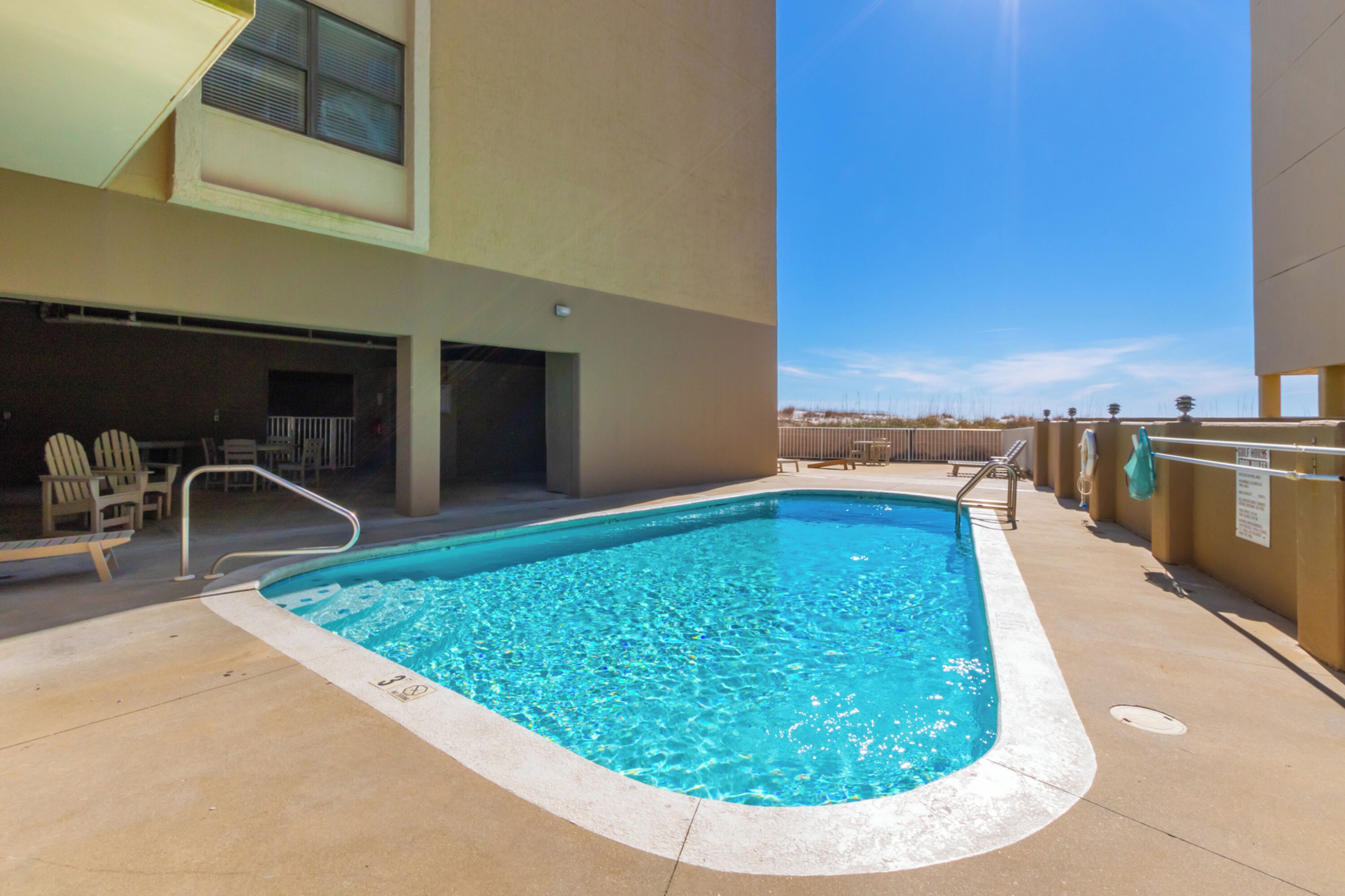 A swimming pool with a metal ladder, surrounded by beige walls and a clear blue sky.