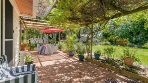 En overdækket terrasse med udendørs møbler, en rød parasol og plantekasser.