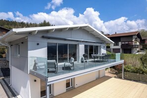 Ein modernes Haus mit einem Glasbalkon, einem Essbereich und Blick auf die umliegende Landschaft.
