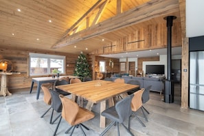 Un intérieur spacieux en bois, avec une grande table à manger, des sièges modernes, un téléviseur et une cheminée.