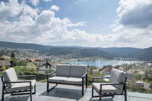 Un balcon avec deux chaises et une table, d’où l’on a vue sur un lac et la ville.