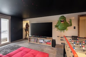 Un salon équipé d’un téléviseur à écran plat, d’un baby-foot et d’une grande décoration représentant un monstre vert accrochée au mur.