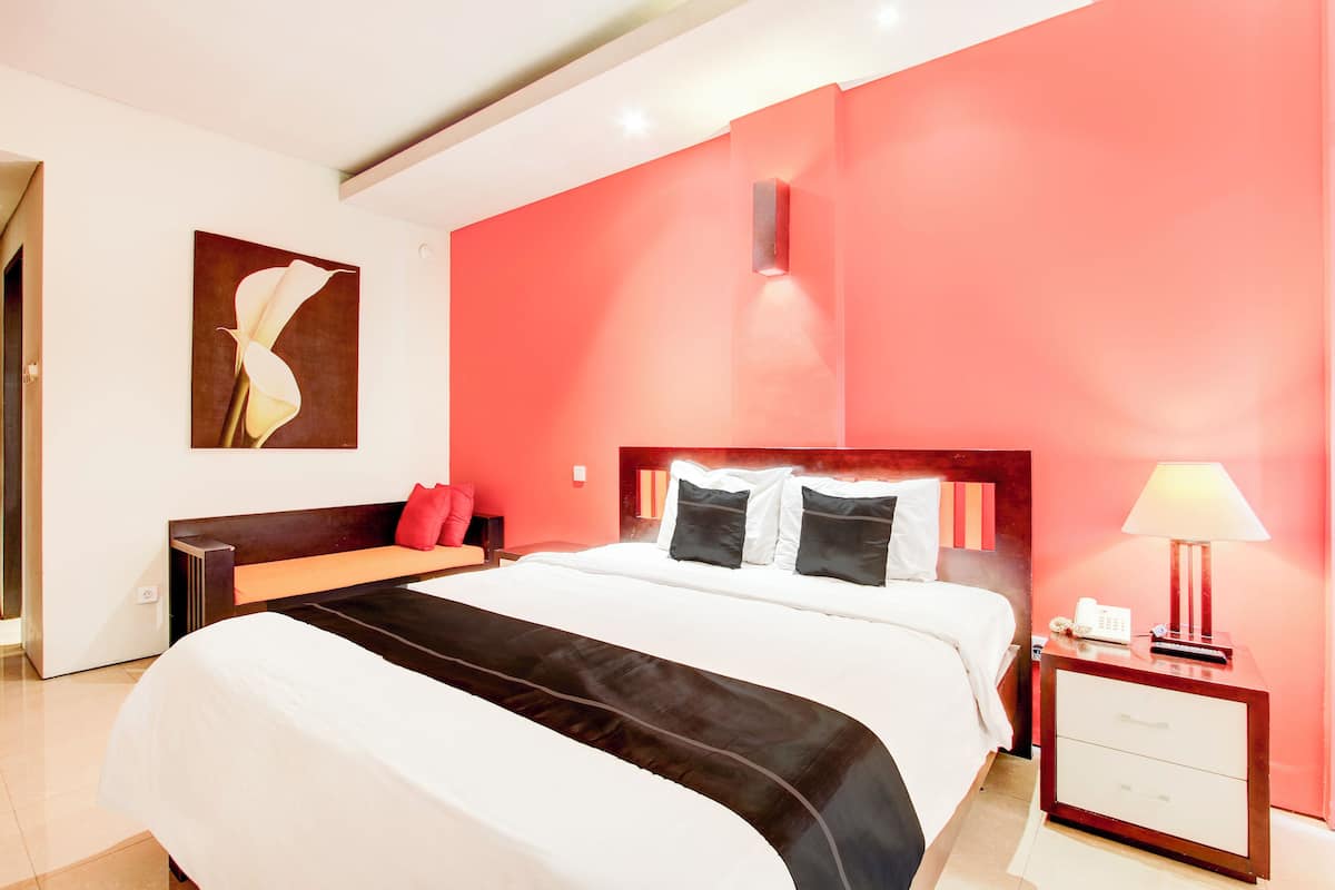 Quarto de hotel com uma cama grande, uma mesa de cabeceira com abajur e um quadro na parede.