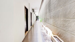 A narrow, clean corridor with a tiled floor, a planter with plants, and a door on the left.