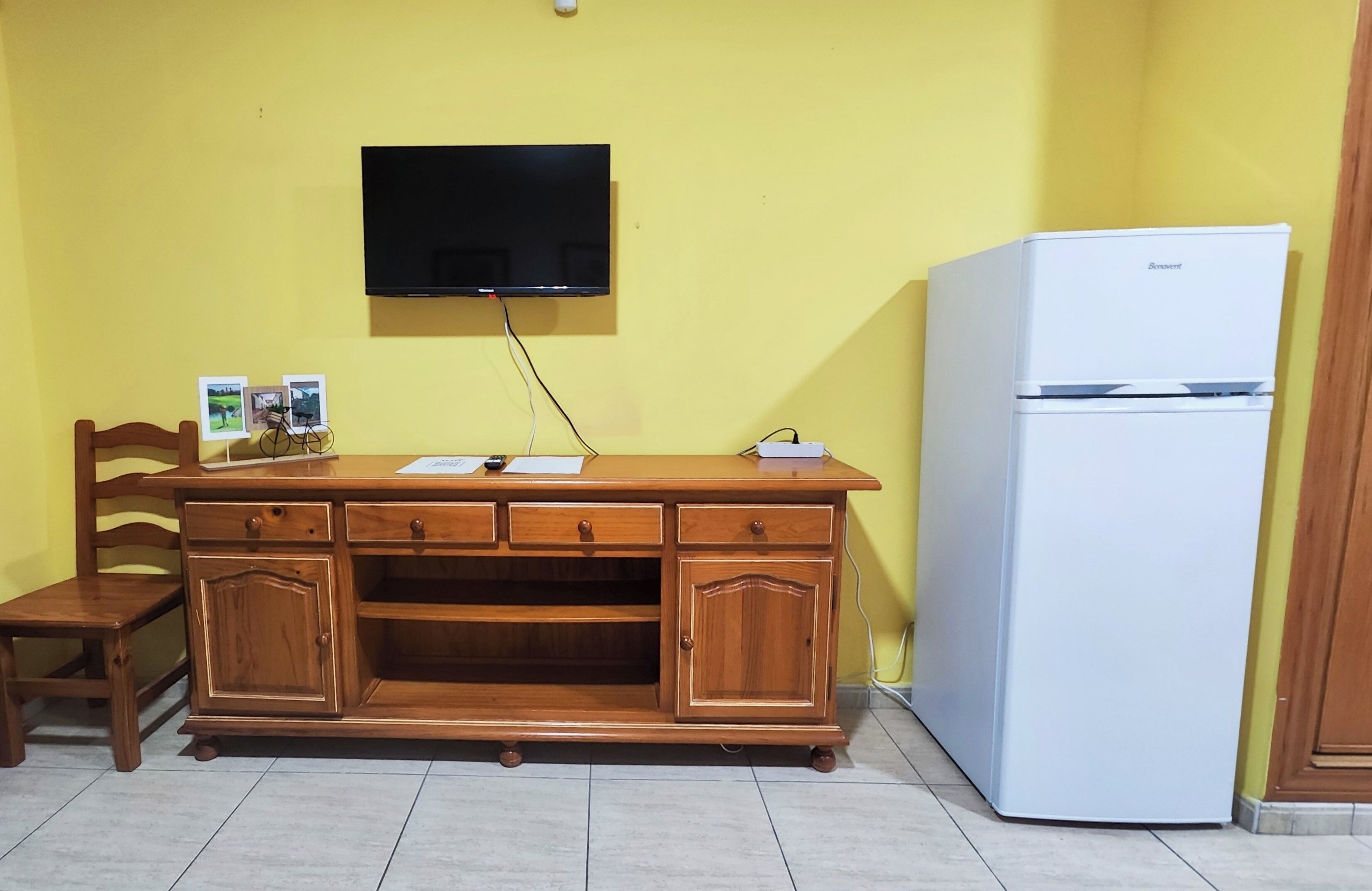 A wooden cabinet with drawers, a television mounted on the wall, and a white refrigerator.