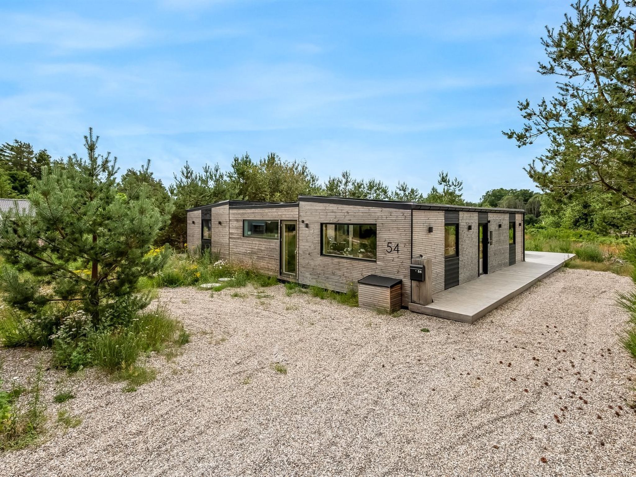 Un moderno chalet a un piano con vialetto sterrato, ampie finestre e il numero '54' sul lato.