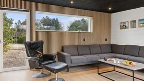 Una sala de estar moderna con un sofá seccional gris, un sillón de cuero negro y una mesita con fruteros.