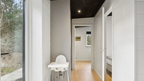 Un pasillo estrecho con una silla blanca, piso de madera y paredes blancas.
