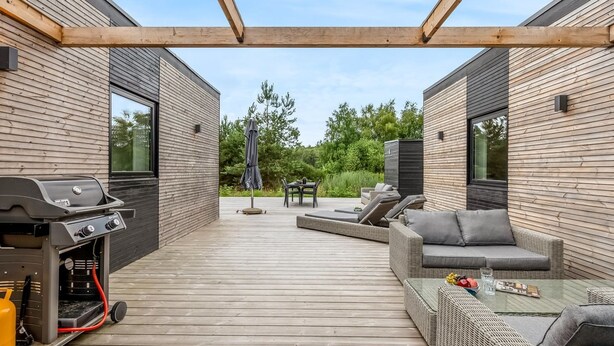 Un patio techado al aire libre con una parrilla, zona de estar y vistas al entorno verde.