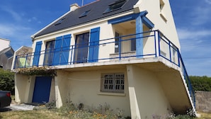 Una casa de dos pisos con un balcón, una puerta azul y una ventana pequeña.
