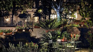 A garden with a table and chairs, surrounded by various plants and flowers.