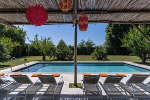 A pool area with lounge chairs and a pergola with hanging lanterns.
