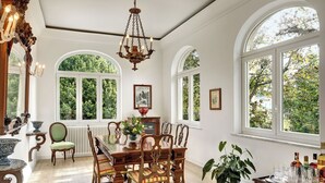 A dining room with a wooden table and chairs, large arched windows, and a chandelier.