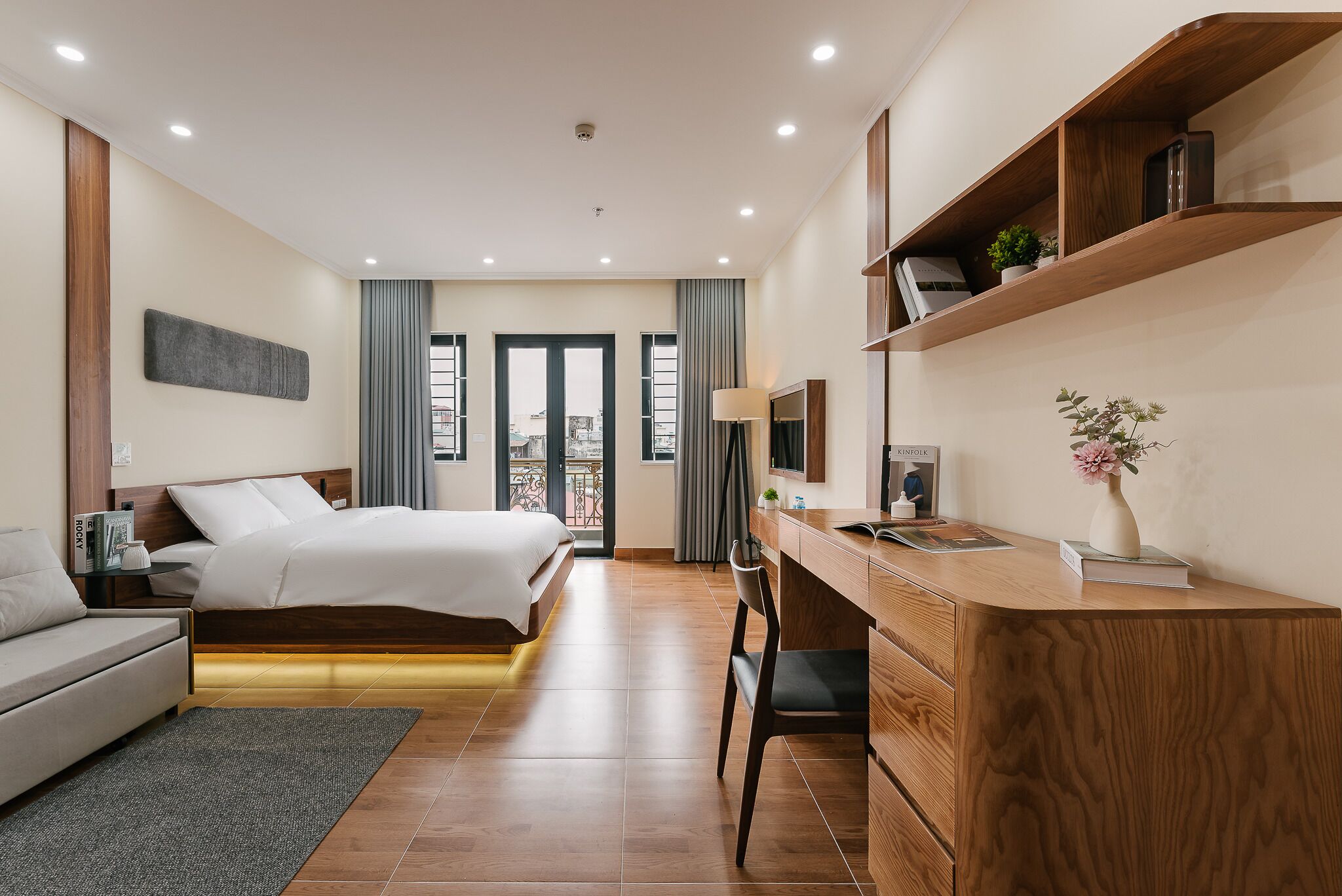 A modern hotel room with a bed, a desk, a chair, a sofa, and a TV.