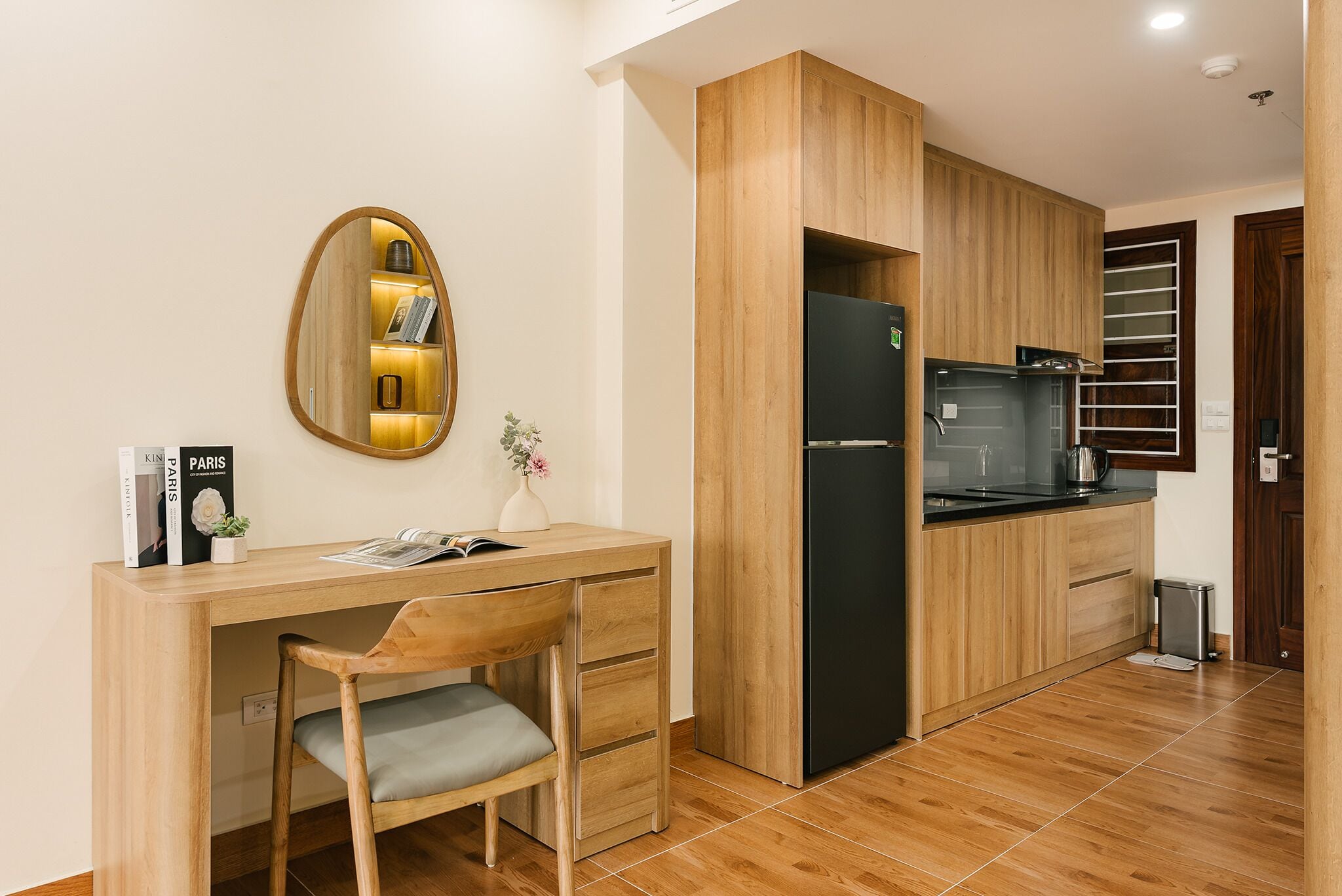 A compact kitchen with a built-in refrigerator, wooden cabinets, and a small dining area with a chair.
