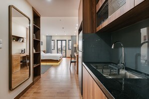 A modern hotel room with a large mirror, wooden furniture, a bed, a desk, and a kitchen area with a sink and stove. - Railway Apartment (Hanoi)