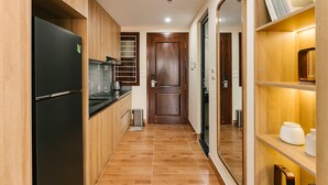 A narrow kitchen with wooden cabinets, a black refrigerator, and a small trash bin.