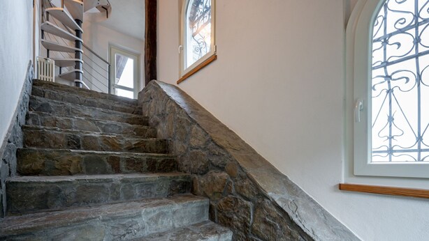 Un escalier en pierre avec une rampe en bois menant à une porte.