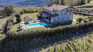 Une maison à deux étages avec une piscine, entourée d’un paysage vallonné et de vignobles.