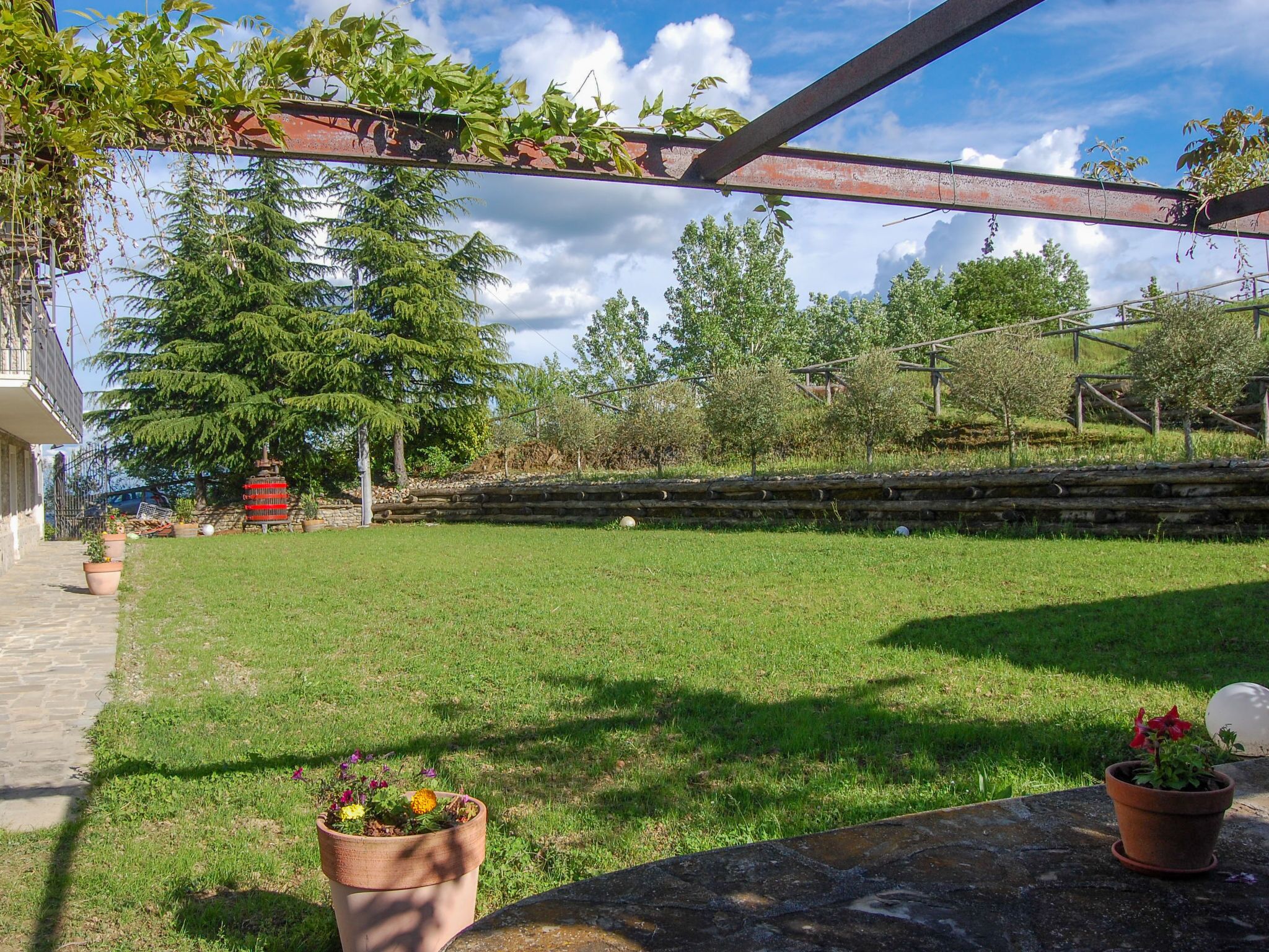 A grassy backyard with a stone wall, potted plants, and a metal structure.