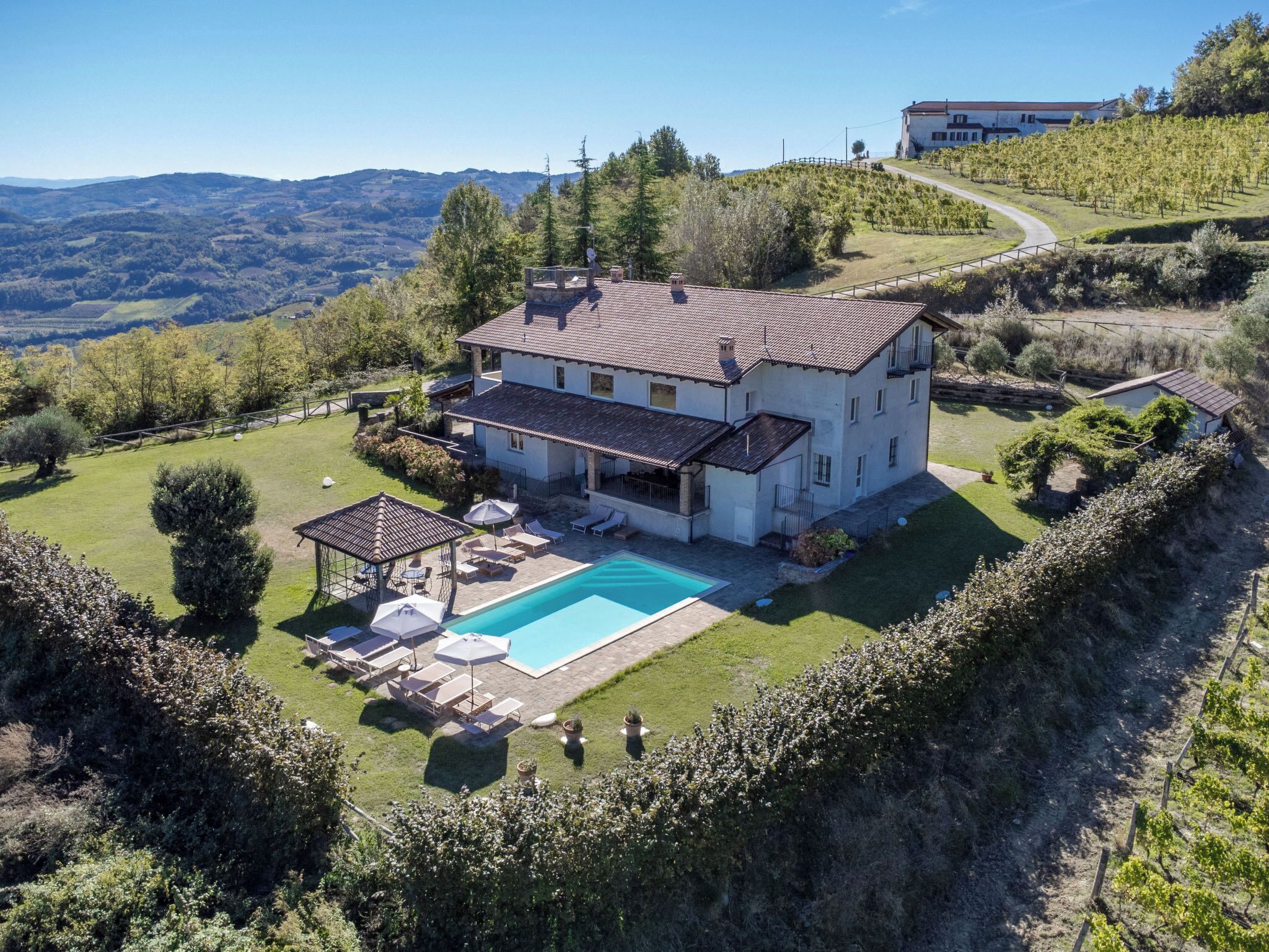 A two-story house with a swimming pool, surrounded by a well-maintained lawn and a vineyard.