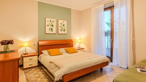 A bedroom with a wooden bed, two bedside tables, a nightstand, a patterned rug, and two wall-mounted lamps. - Apartment Paníco by Interhome (Dorio)