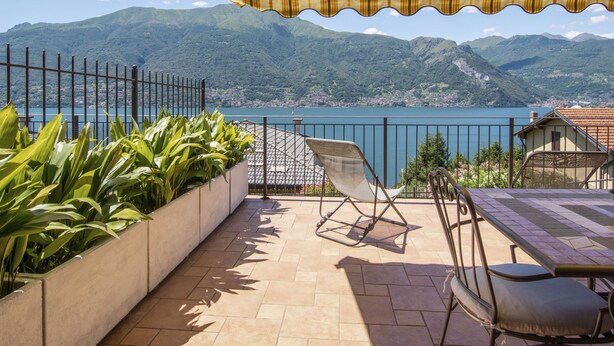 A terrace with a view of a lake and mountains, featuring a table, chairs, and potted plants. - Apartment Paníco by Interhome (Dorio)