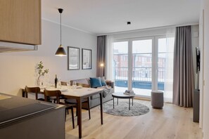 A modern apartment with a dining area, a sofa, a small round table, and large windows offering a view of the city. - Arbio I Makro Apartments Classical (Hamburg)