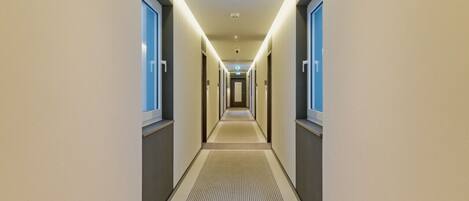 A modern hotel hallway with a central carpeted walkway, flanked by doors on both sides.