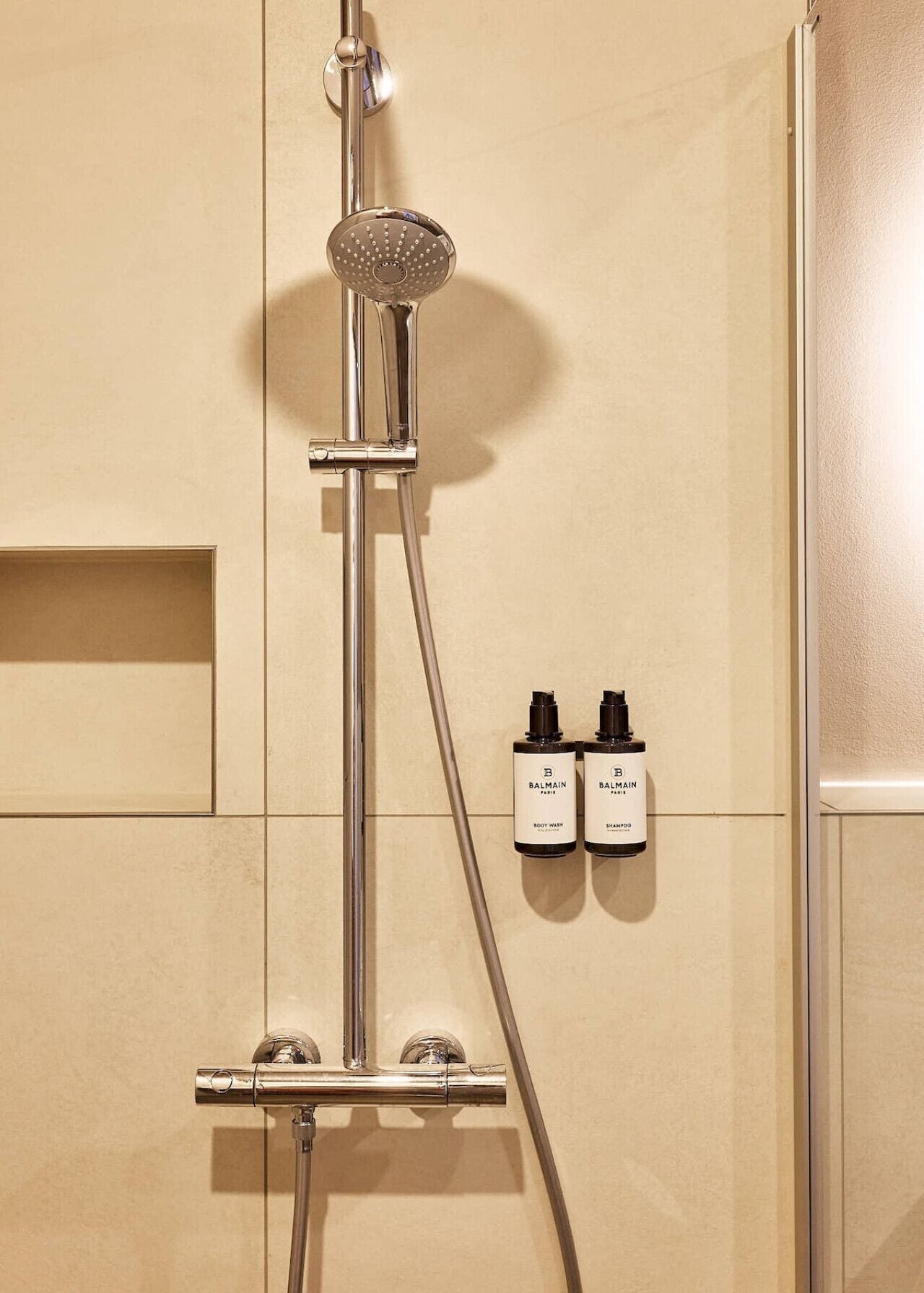 A shower with a handheld showerhead and two bottles of Balmain body wash and shampoo.