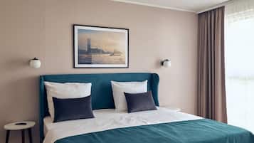 Habitación de hotel con cabecera color turquesa, ropa de cama blanca y una pintura de un paisaje urbano en la pared.