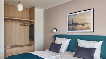 Quarto de hotel com cama, guarda-roupa, quadro na parede e luminária pendente.