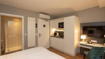 Une chambre d’hôtel comprenant un lit, un bureau avec une chaise, une télévision, une petite kitchenette et une salle de bain avec douche et toilettes.