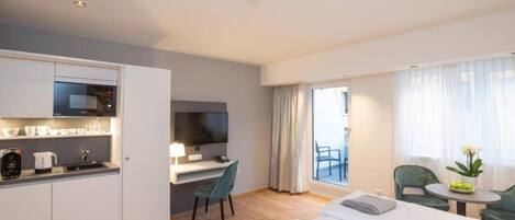 Et lille hotelværelse med tekøkken, seng, skrivebord med TV og balkon med udsigt.