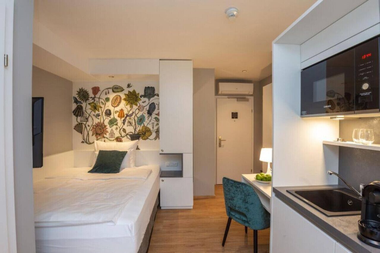 Et lille hotelværelse med seng, et skrivebord med stol, et tekøkken og en væg med et blomstermotiv.