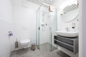Moderni kylpyhuone, jossa on lasiseinällä varustettu suihku, valkoinen pesuallas ja wc.