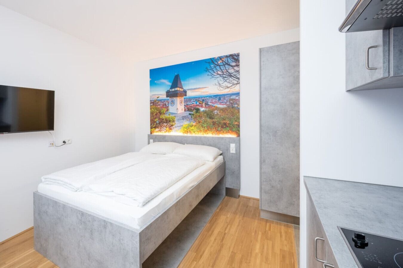 A modern room with a bed, a TV mounted on the wall, and a painting of a cityscape.