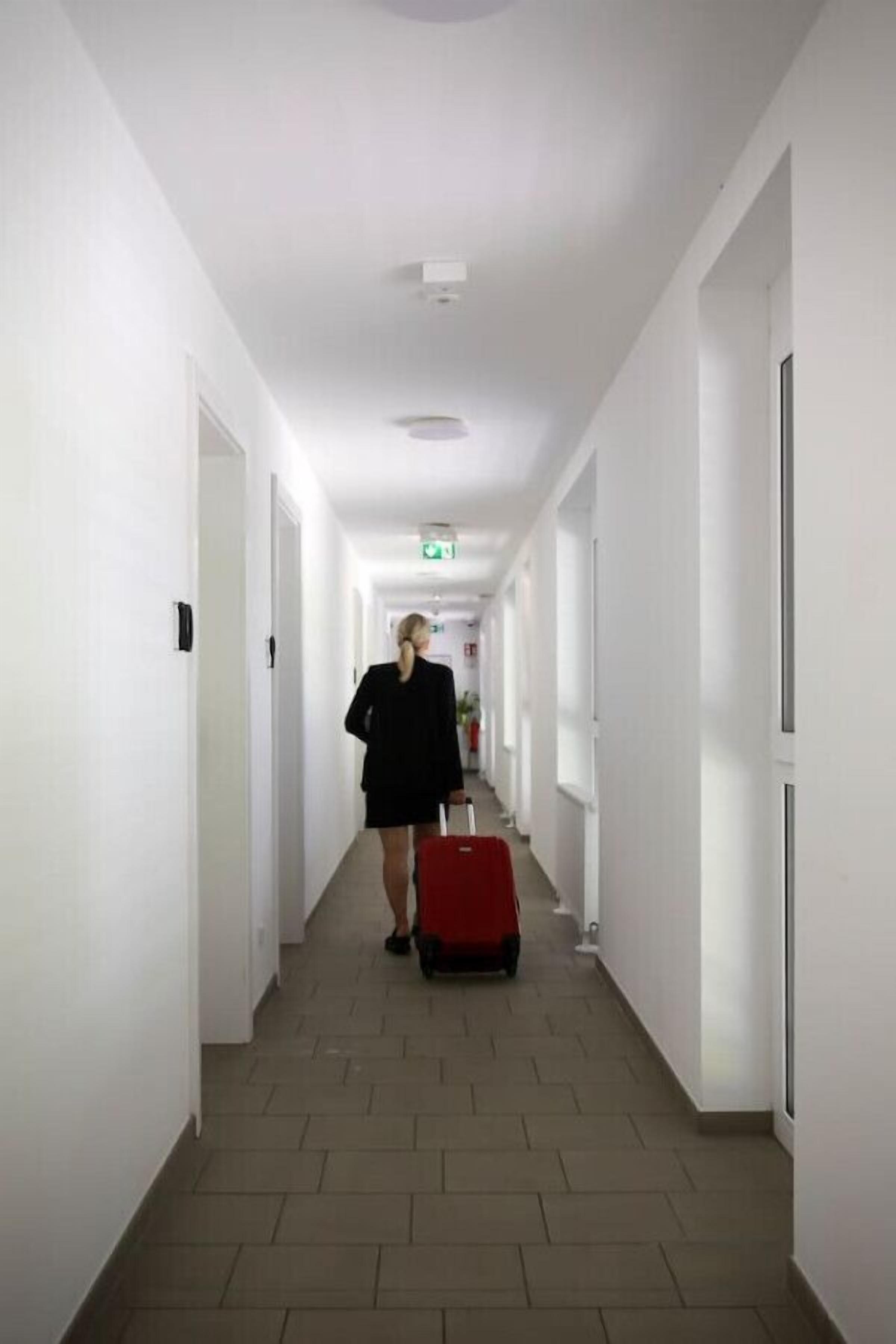 A hotel corridor with white walls, a tiled floor, and doors on both sides.