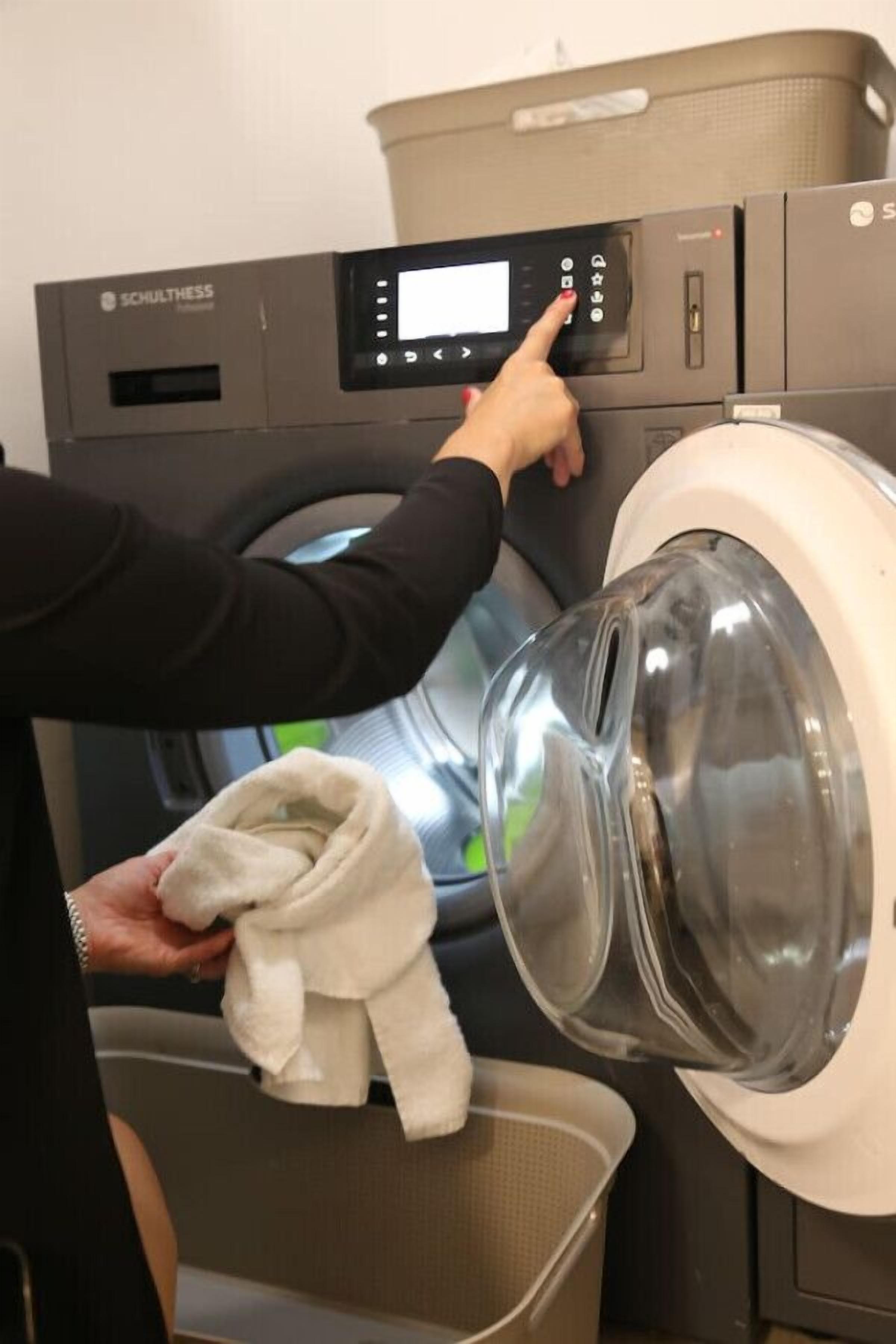 A person operating a SCHULTHESS washing machine, with a transparent drum and a control panel.
